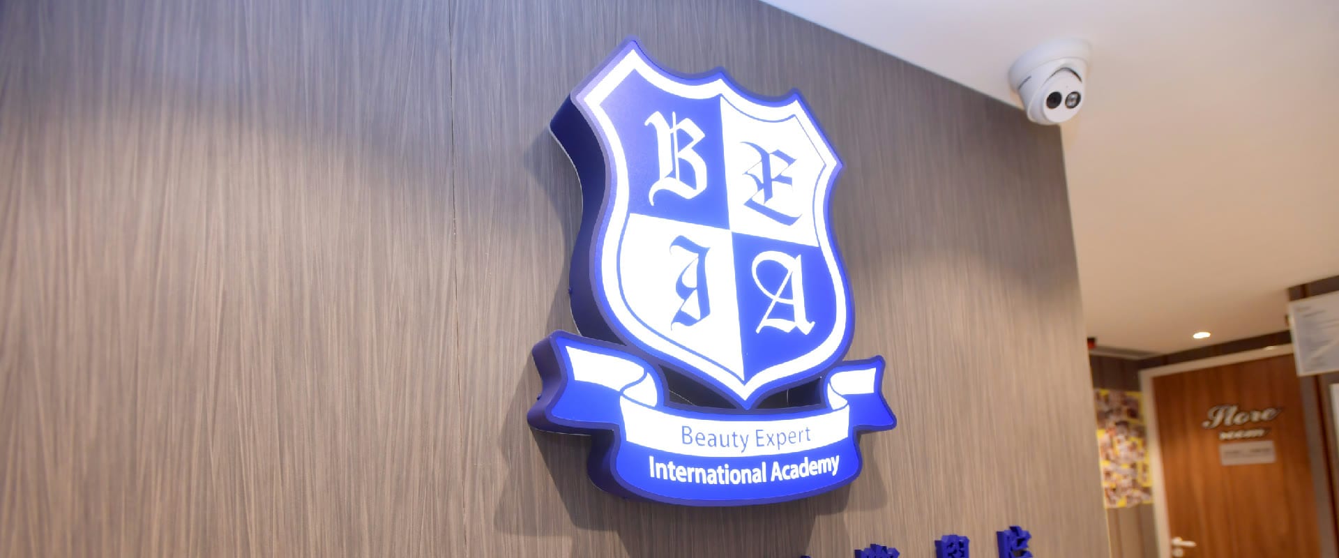 美容專家國際學院校舍牆上的學院盾徽立體標誌,下方橫幅寫有 Beauty Expert International Academy